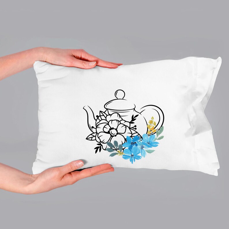 May include: A white pillow with a black line drawing of a teapot with blue and yellow flowers.