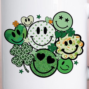 May include: White ceramic mug with a green, yellow, and black design of smiling faces, shamrocks, and stars.