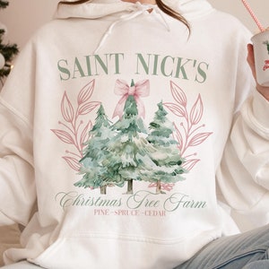 May include: White hoodie with a watercolor design featuring Christmas trees and the text "SAINT NICK'S CHRISTMAS TREE FARM". The design includes a pink bow and leaves. The hoodie also has the text "PINE - SPRUCE - CEDAR".
