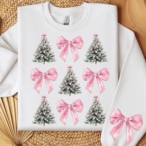 May include: White sweatshirt featuring a pattern of pink bows and Christmas trees. The design includes nine trees and bows, with a single bow on the sleeve. The trees are green with pink ornaments. The bows are a soft pink color.