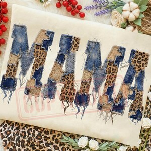 May include: A cream-colored graphic featuring the word "MAMA" in a patchwork design. The letters are composed of denim, leopard print, and tan fabric, with frayed edges. The design is surrounded by floral and decorative elements.