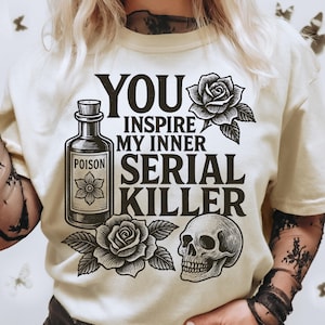 May include: Cream-colored t-shirt with the text "YOU INSPIRE MY INNER SERIAL KILLER." The design includes a poison bottle, roses, and a skull. The shirt has short sleeves.
