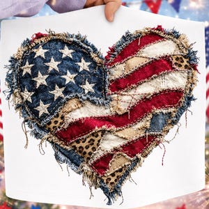Op de afbeelding: Een hartvormig ontwerp met de Amerikaanse vlag, in een distressed, patchwork-stijl. Het ontwerp bevat denim, rood-witte strepen en luipaardprint accenten. De randen hebben een gerafeld, rustiek uiterlijk en het ontwerp wordt door een persoon vastgehouden.