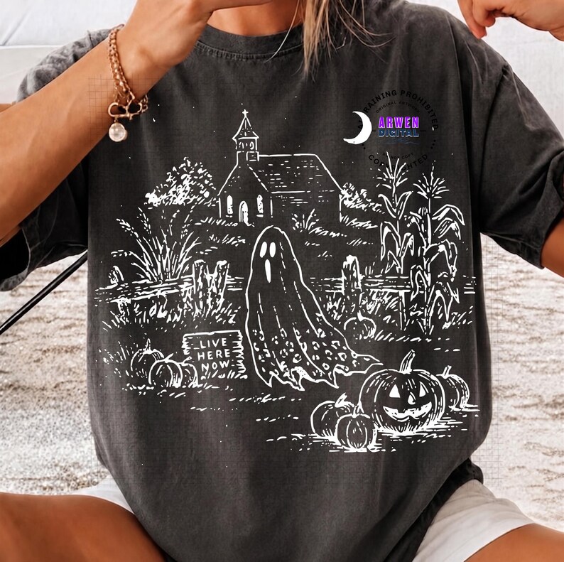 May include: A charcoal gray t-shirt featuring a white line art graphic of a haunted scene with a church, a ghost, corn stalks, and pumpkins. A sign in the graphic reads "LIVE HERE NOW". The design includes a crescent moon and circular text.