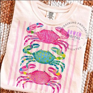 Puede incluir: Camiseta de color melocot&oacute;n claro con un dise&ntilde;o de tres cangrejos coloridos. Los cangrejos son rosas, azules y amarillos con ilustraciones detalladas al estilo acuarela. Rayas rosas verticales en la camiseta. El texto "ARWEN DIGITAL" es visible.