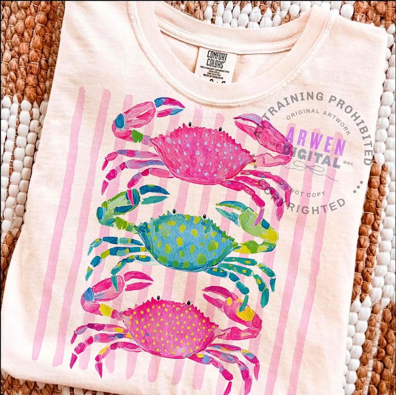 Puede incluir: Camiseta de color melocot&oacute;n claro con un dise&ntilde;o de tres cangrejos coloridos. Los cangrejos son rosas, azules y amarillos con ilustraciones detalladas al estilo acuarela. Rayas rosas verticales en la camiseta. El texto "ARWEN DIGITAL" es visible.