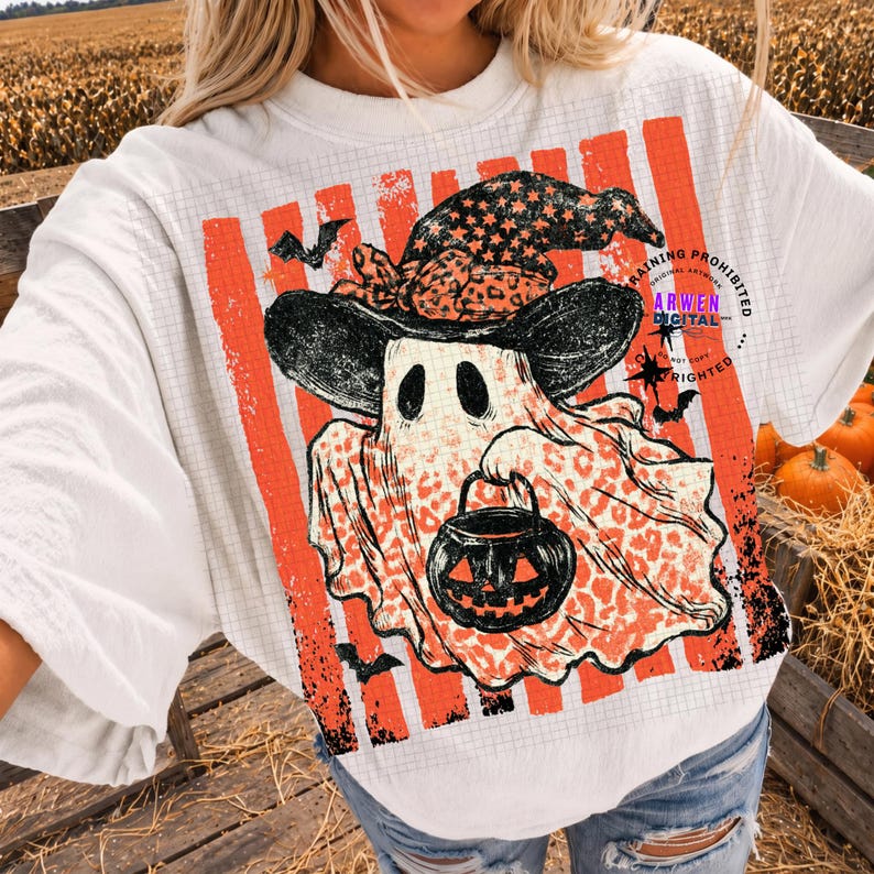 May include: A white t-shirt featuring a graphic of a ghost wearing a black witch hat with orange star patterns. The ghost has a leopard print body and holds a black jack-o'-lantern bucket. The background includes orange vertical stripes.