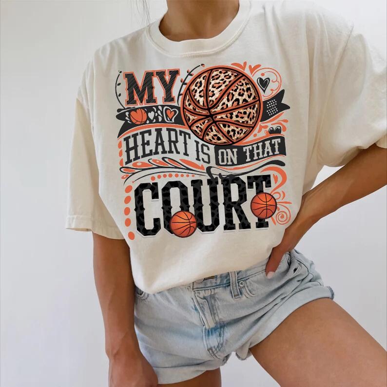 May include: A white t-shirt featuring a graphic print of a basketball with a leopard print design. The text on the shirt reads "My heart is on that court".