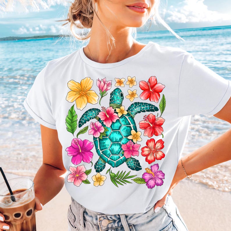 May include: White t-shirt featuring a colourful graphic of a sea turtle surrounded by tropical flowers. The turtle is turquoise blue with a yellow shell and pink, orange, and yellow flowers.