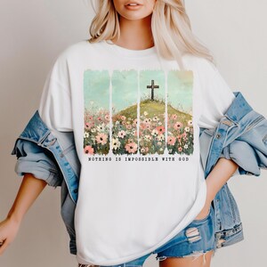 May include: White t-shirt with a graphic of a cross on a hill with flowers. The text "NOTHING IS IMPOSSIBLE WITH GOD" is printed below the graphic.