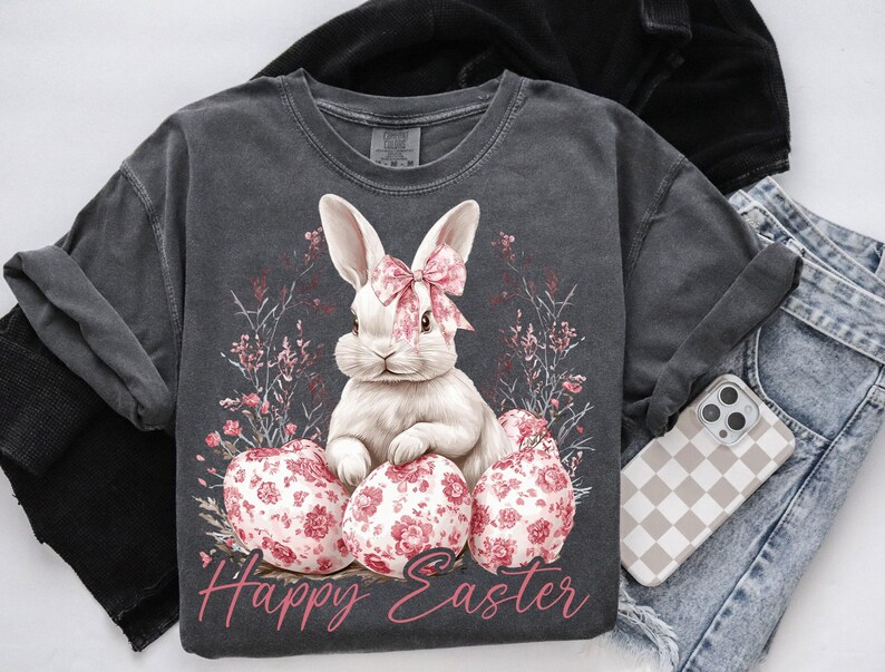 May include: A gray t-shirt with a white bunny rabbit holding pink Easter eggs. The bunny has a pink bow around its neck. The shirt has the text "Happy Easter" printed on it.