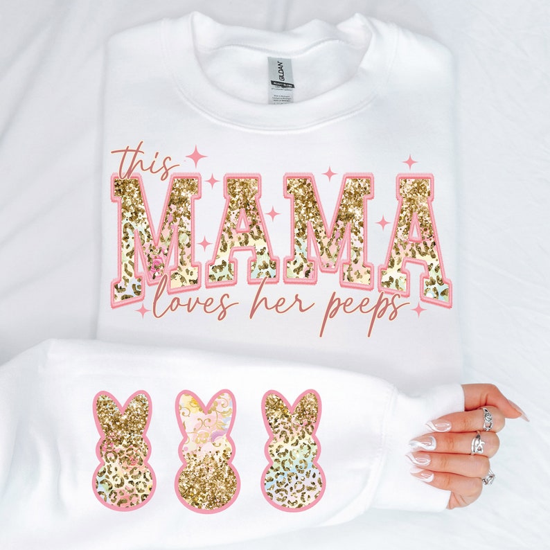 以下が含まれることがあります： ピンクのグリッター文字で「This Mama loves her peeps」と書かれた白いスウェットシャツ。文字の下には、ピンクのグリッターでできたピープバニーが3匹います。