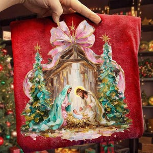 May include: Red Christmas stocking with a Nativity scene illustration. The artwork depicts Mary, Joseph, and baby Jesus in a manger, framed by Christmas trees. A large pink bow adorns the top of the stocking.