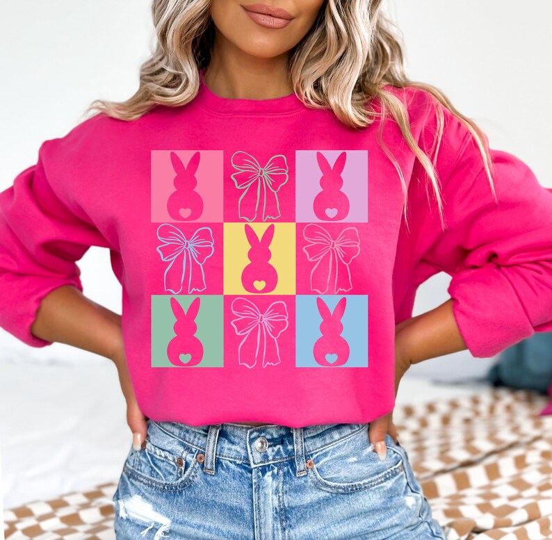 May include: A pink sweatshirt with a colorful pattern of bunnies and bows. The pattern is made up of nine squares, each with a different color and design.