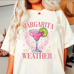 May include: White t-shirt featuring a pink margarita graphic and the text "Margarita Weather" with the words "Est. 1862" below the graphic.