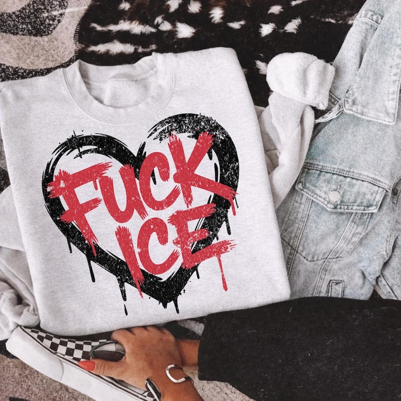 May include: A light gray sweatshirt with a black heart design and the words "FUCK ICE" in red. The design has a distressed, grunge style with dripping paint effects. The sweatshirt is paired with denim and a checkered shoe.