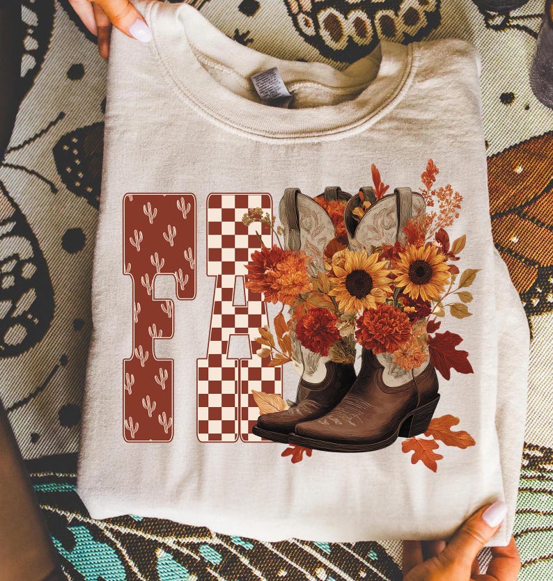 May include: A cream-colored sweatshirt featuring the word "FA" in a western-style font with cactus and checkered patterns. The design includes brown cowboy boots, sunflowers, and fall foliage. The overall theme is autumn and country.