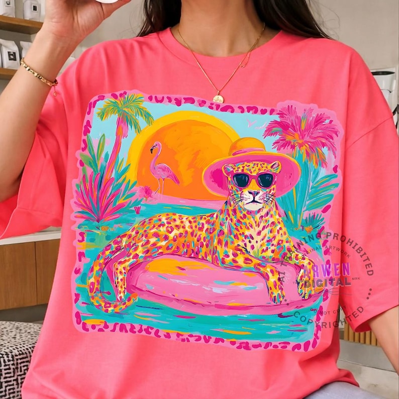 K&ouml;nnte beinhalten: Hellrosa T-Shirt mit einer farbenfrohen Illustration eines Leoparden mit Sonnenbrille und Hut, der auf einem rosa Schwimmreifen liegt. Die Grafik zeigt einen Sonnenuntergang, Palmen und einen Flamingo. Ein lebendiges, auff&auml;lliges Design.