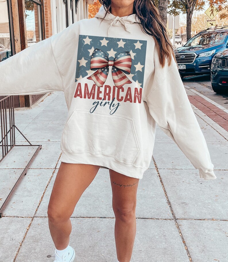 May include: A cream-colored hoodie with a vintage-style American flag bow and the text "AMERICAN girly".