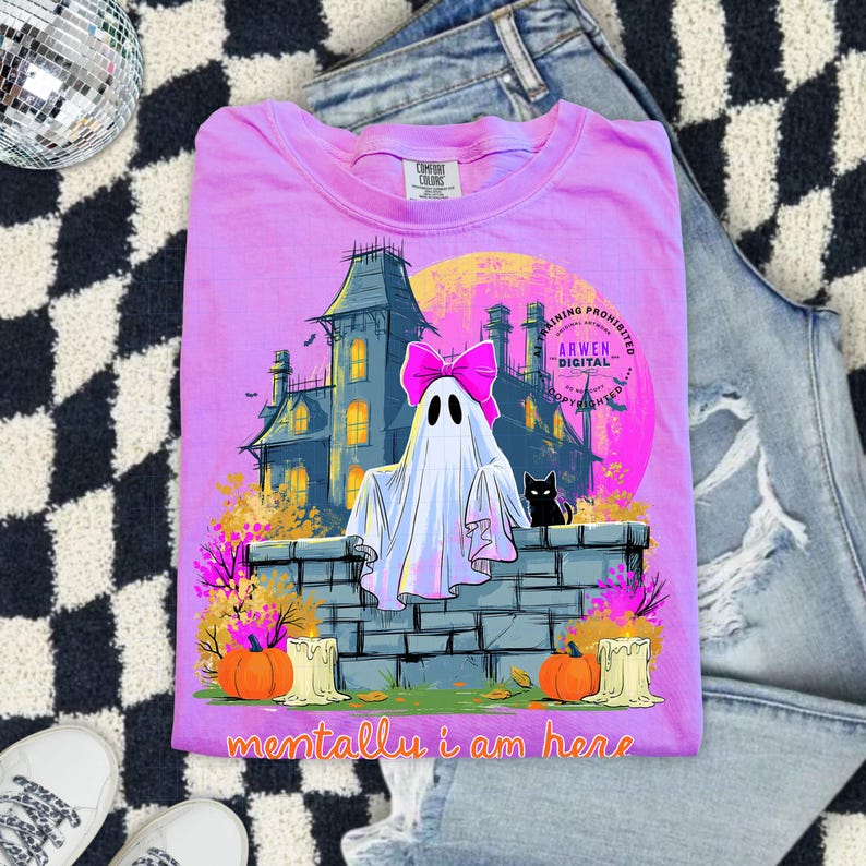 Puede incluir: Una camiseta de color morado claro con un gr&aacute;fico de un fantasma con un lazo rosa, un gato negro, una casa encantada, calabazas y velas. El texto "mentally i am here" est&aacute; impreso en la parte inferior, con "ARWEN DIGITAL" cerca de la luna.