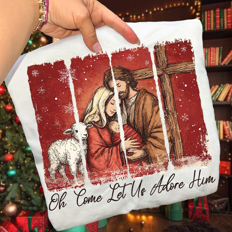 May include: White pillow with a religious illustration featuring a family, a lamb, and a cross, set against a red background with snowflakes. The text "Oh Come Let Us Adore Him" is at the bottom.