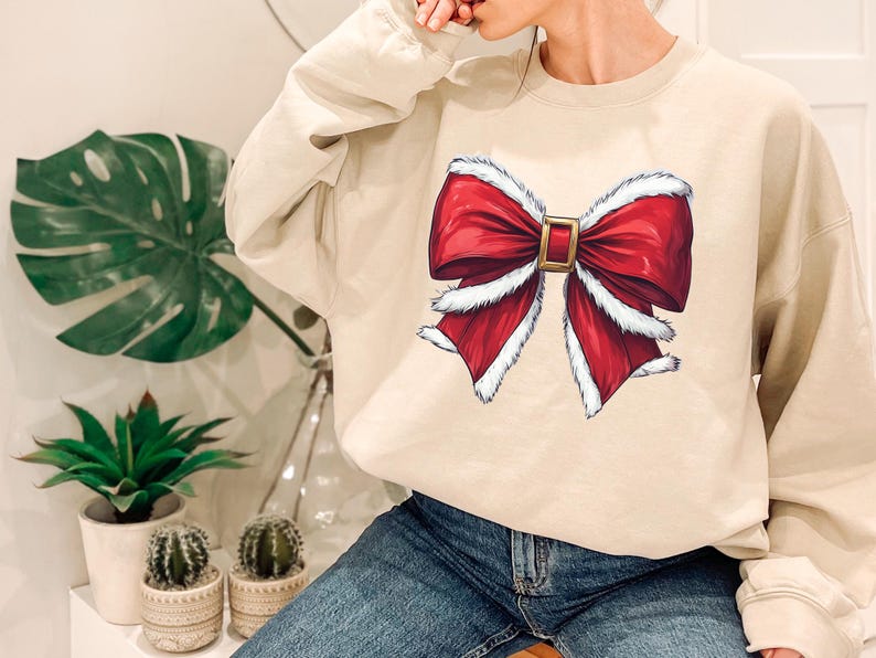 Puede incluir: Sudadera beige de cuello redondo con un gran dise&ntilde;o de lazo rojo con ribete blanco y hebilla dorada. El lazo es un gr&aacute;fico festivo, perfecto para la temporada navide&ntilde;a. La sudadera es de color neutro, adecuada para varios conjuntos.