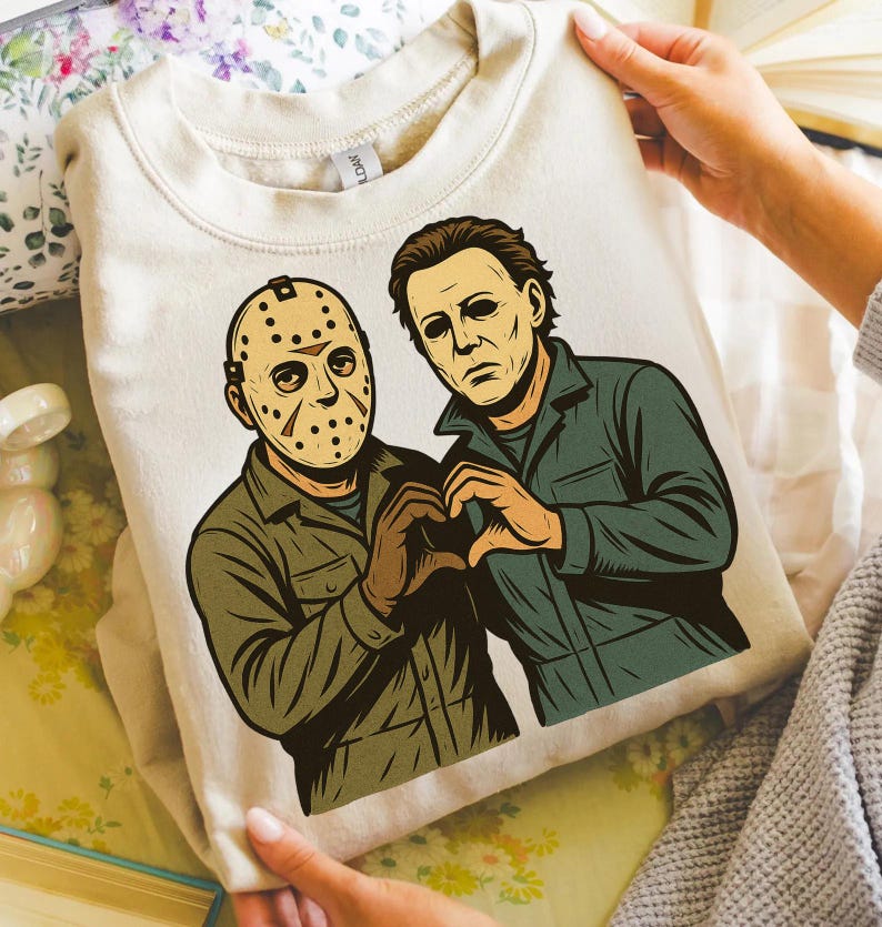 May include: A cream-colored sweatshirt featuring a graphic of two horror movie characters, Jason Voorhees and Michael Myers, forming a heart shape with their hands. The artwork is in a vintage comic book style, with the characters in their signature outfits.