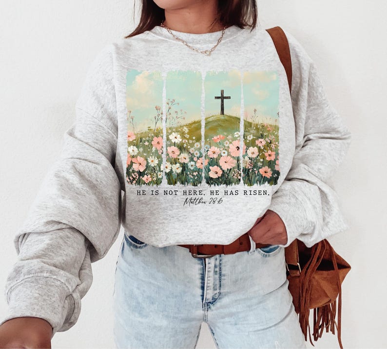 May include: A gray sweatshirt with a floral design and a cross on a hill. The text "He is not here. He has risen. Matthew 28:6" is printed on the sweatshirt.