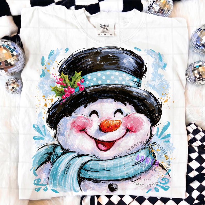 May include: A white t-shirt featuring a graphic illustration of a smiling snowman wearing a black top hat with a light blue polka dot band, a light blue scarf, and a sprig of holly with red berries. The snowman has rosy cheeks and an orange nose.