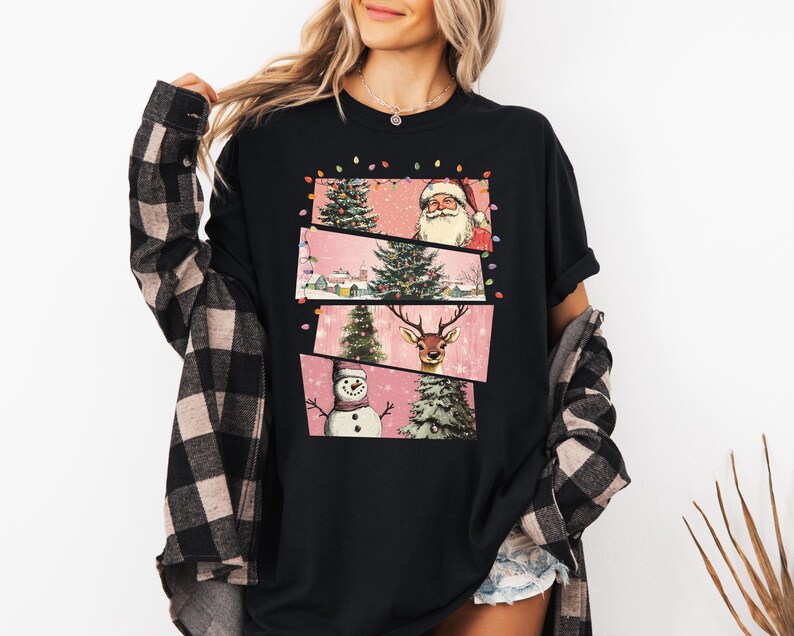 May include: Black t-shirt featuring a festive Christmas design. The graphic includes Santa Claus, a reindeer, a snowman, and Christmas trees. The design is set against a pink background with string lights.
