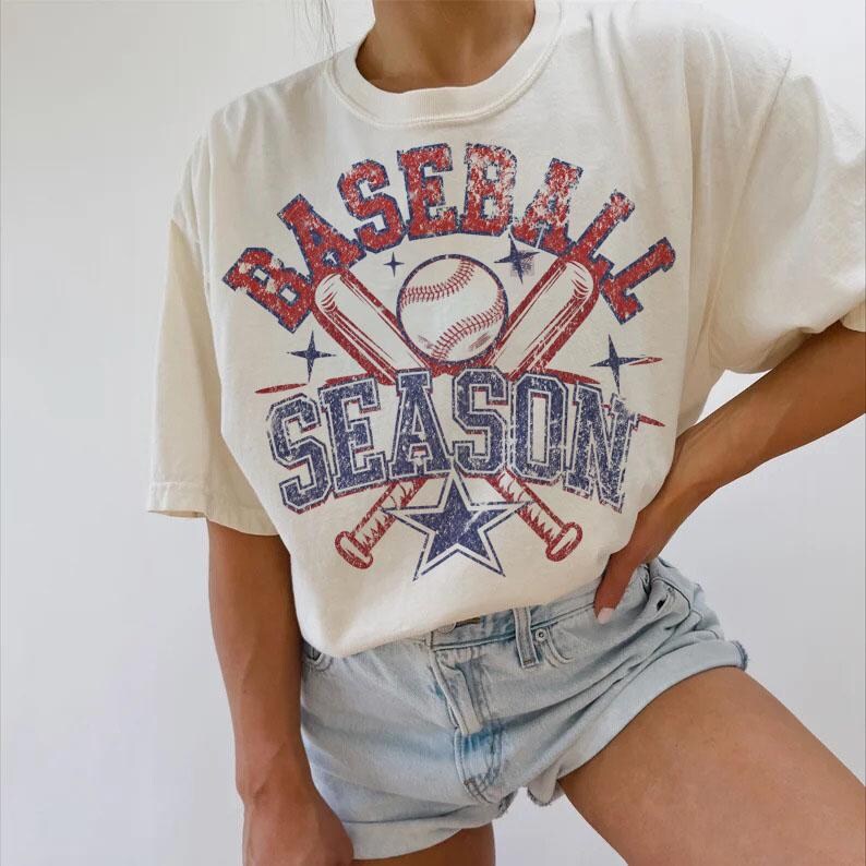 May include: A white t-shirt with a vintage baseball graphic. The graphic features two crossed baseball bats, a baseball, and the text "Baseball Season".