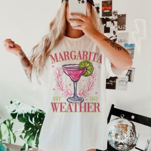 May include: White t-shirt featuring a pink margarita graphic and the text "Margarita Weather" with "Est. 1862" underneath.
