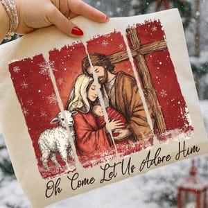 May include: A beige tote bag featuring a religious illustration with a red background and a wooden cross. The image depicts a family with a baby, a lamb, and the text "Oh Come Let Us Adore Him". Snowflakes are scattered throughout the design.