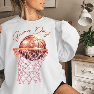 May include: White sweatshirt with a pink and gold basketball hoop and basketball with the text "Game Day" on the front.