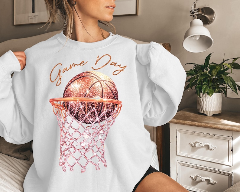 May include: White sweatshirt with a pink and gold basketball hoop and basketball with the text "Game Day" on the front.