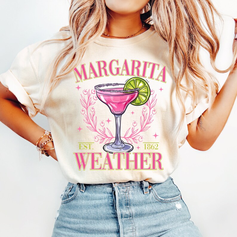 May include: A white t-shirt with a pink margarita glass and lime wedge graphic. The text "Margarita Weather" is printed on the shirt with the words "Est. 1862" below the graphic.