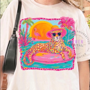 K&ouml;nnte beinhalten: Cremefarbenes T-Shirt mit einem farbenfrohen Grafikdesign. Es zeigt einen Leoparden mit Sonnenbrille und rosa Hut, der auf einem rosa aufblasbaren Ring liegt. Das Design umfasst einen Sonnenuntergang, Palmen und einen Flamingo.