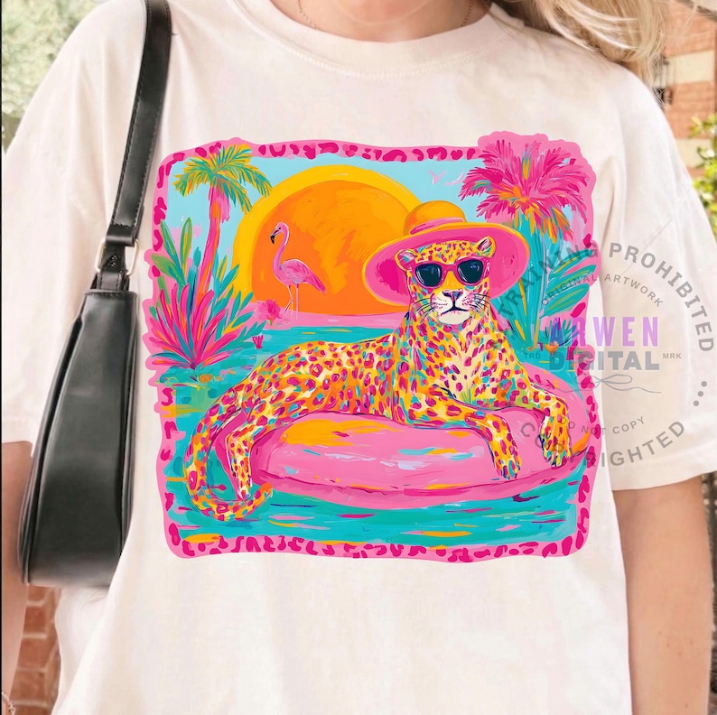 K&ouml;nnte beinhalten: Cremefarbenes T-Shirt mit einem farbenfrohen Grafikdesign. Es zeigt einen Leoparden mit Sonnenbrille und rosa Hut, der auf einem rosa aufblasbaren Ring liegt. Das Design umfasst einen Sonnenuntergang, Palmen und einen Flamingo.