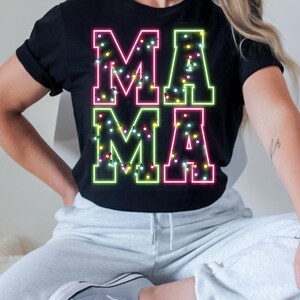 May include: Black t-shirt with the word "MAMA" in neon pink and green. The letters are outlined with a bright neon glow and decorated with tiny, colorful lights. A casual, festive design.