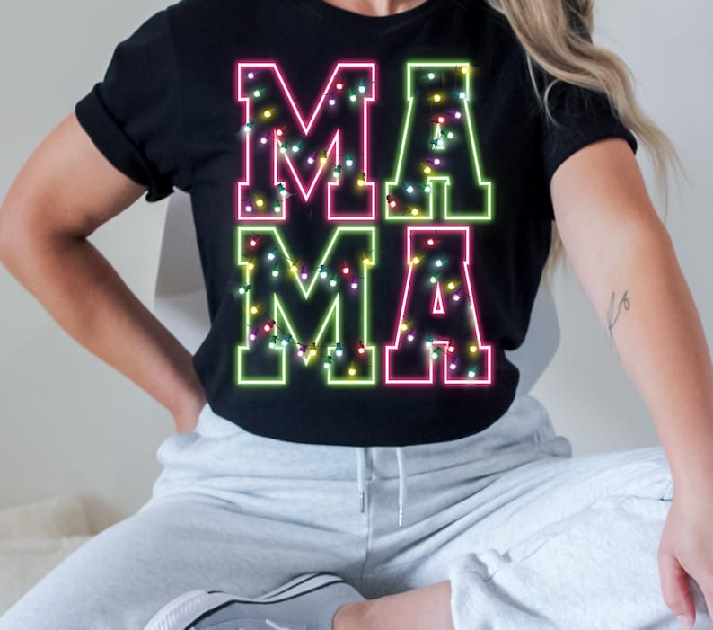 May include: Black t-shirt with the word "MAMA" in neon pink and green. The letters are outlined with a bright neon glow and decorated with tiny, colorful lights. A casual, festive design.