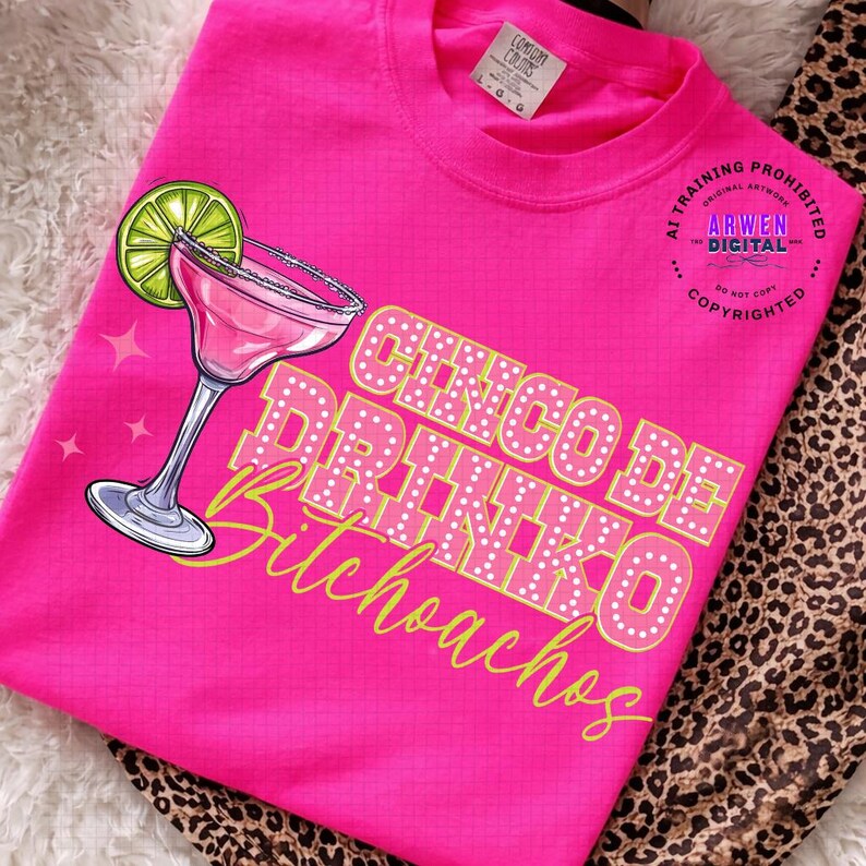 May include: A bright pink t-shirt featuring a margarita glass with a lime wedge and the text "Cinco De Drinko Bitchoachos" in a playful font. The shirt has a crew neck and short sleeves.
