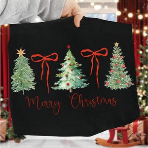 May include: Black Christmas-themed tote bag featuring watercolor illustrations of three decorated Christmas trees with red bows and the text "Merry Christmas" in red script. The trees are adorned with ornaments and topped with stars.