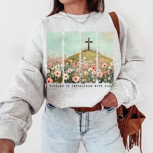 May include: A gray sweatshirt with a graphic print of a cross in a field of flowers. The text "Nothing is impossible with God" is printed below the image.