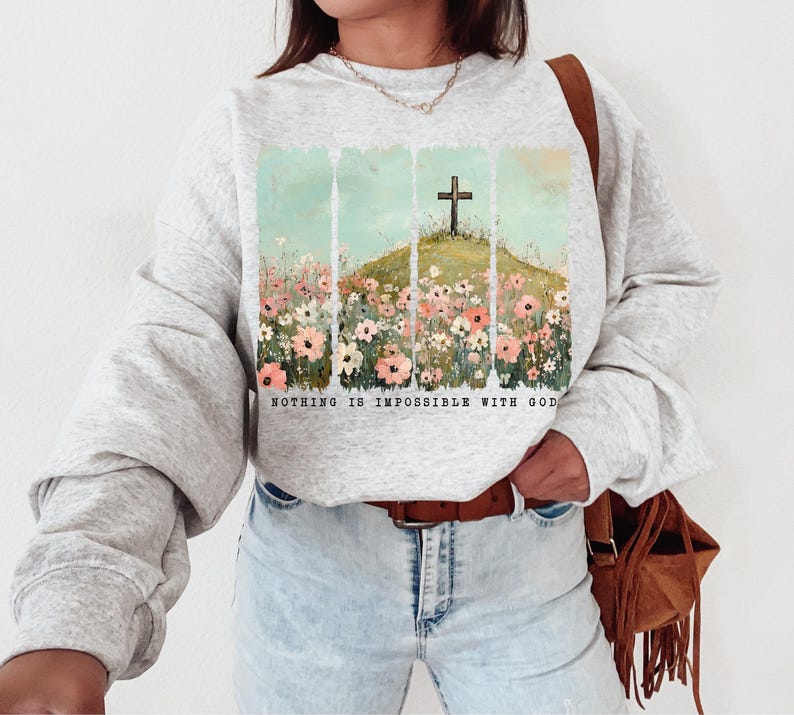 May include: A gray sweatshirt with a graphic print of a cross in a field of flowers. The text "Nothing is impossible with God" is printed below the image.
