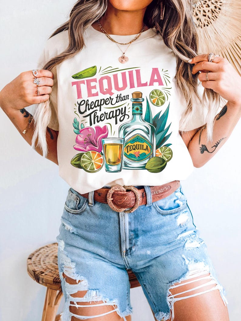 Pu&ograve; includere: Maglietta bianca con un design grafico di una bottiglia di tequila, un bicchierino, lime e fiori. Il testo sulla maglietta recita "Tequila Cheaper than Therapy".