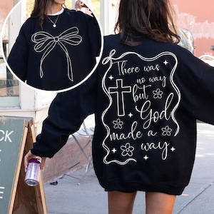 Puede incluir: Sudadera negra con un lazo blanco en la parte delantera y el texto "There was no way but God made a way" con una cruz y flores en la parte posterior.