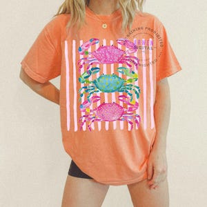 Puede incluir: Camiseta naranja con un patr&oacute;n de rayas blancas verticales y tres ilustraciones de cangrejos coloridos. Los cangrejos son rosas, azules y rosas, con dise&ntilde;os detallados de acuarela. La camiseta tiene el texto "TRAINING PROHIBITED ARWEN DIGITAL COPYRIGHTED".
