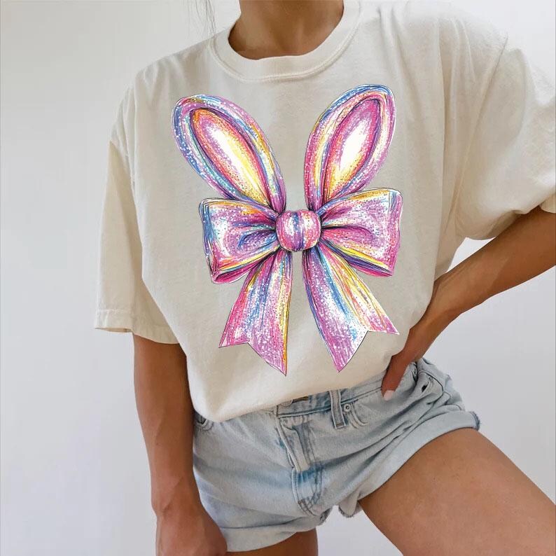 May include: A white t-shirt with a large, colorful, iridescent bow design. The bow is pink, purple, and blue with a white center.