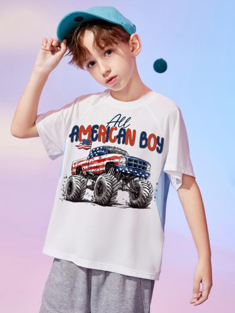 May include: White t-shirt with a graphic of a monster truck decorated with the American flag and the text "All AMERICAN BOY". The shirt has blue accents on the sides and is worn by a person wearing a blue baseball cap.