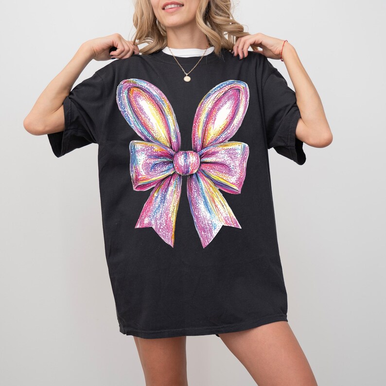 May include: Black oversized t-shirt with a large, colorful, glittery bow graphic.
